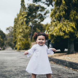 smiling baby girl wearing white dress standing on road
